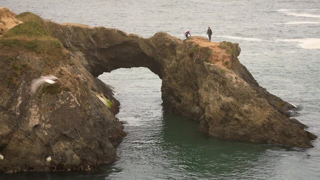 A couple enjoys time at an arch in Mendocino Headlands State Park while taking in the views of the ocean and coastline on a foggy day.