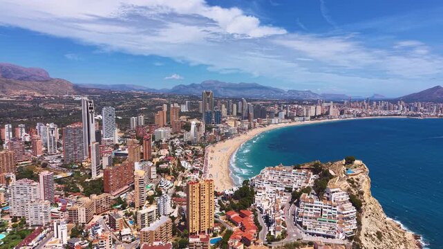 Panoramic aerial view of Benidorm, Spain, showcasing the iconic skyscraper skyline, sandy Levante beach, turquoise Mediterranean Sea, and mountain backdrop