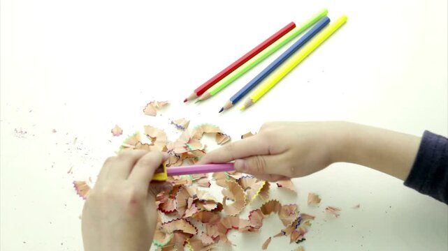 Hands sharpening a colorful pencil with manual sharpener creating wood shavings and sharp tips in 4K Ultra HD footage.
