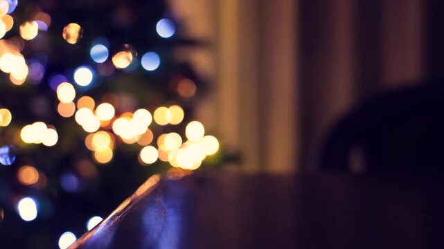 tavolo di legno vuoto in primo piano in interni domestici, bassa profondit&agrave; di campo, albero di natale con addobbi e luci colorate e brillanti sullo sfondo sfuocato e con effetto bokeh
