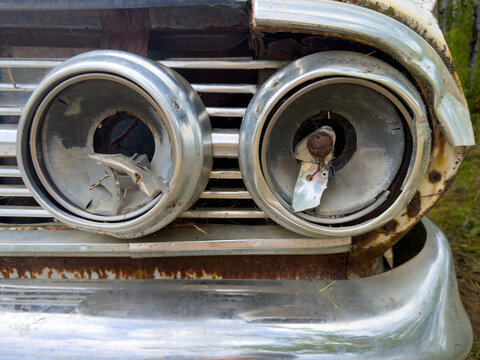 Close-up of two old broken headlights with chrome outlines and bumper
