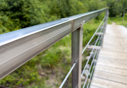 Perspective view along a bright steel railing on a walking trail through a forest. The focus range is very limited

