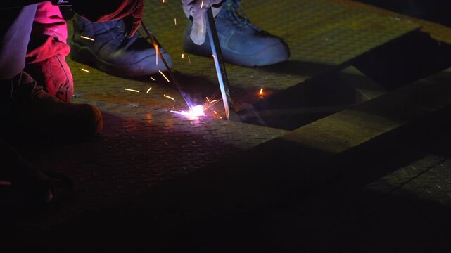 Welder Performing Stick Arc Welding on Metal Floor Surface Close Up With Bright Sparks in Industrial Environment