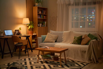 Empty cozy living room with desk, laptop, and sofa at night representing remote work setup. Image suitable for home office design, remote employment, and interior decor marketing © Seventyfour