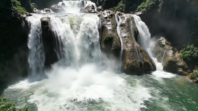 A powerful tropical waterfall cascades down into a lush green pool