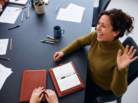 Cheerful businesswoman laughing and waving hand during a team meeting around a conference table in an office