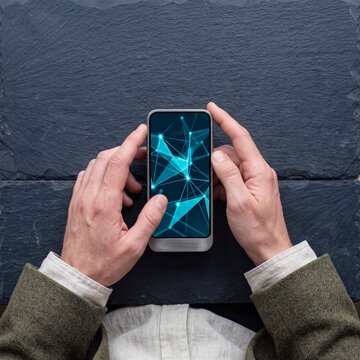 Top view of businessman hands holding smartphone with glowing digital network mesh on screen over dark stone background
