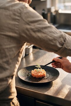 Professional Chef Plating Gourmet Salmon Tartare Dish with Culinary Tweezers in Restaurant Kitchen