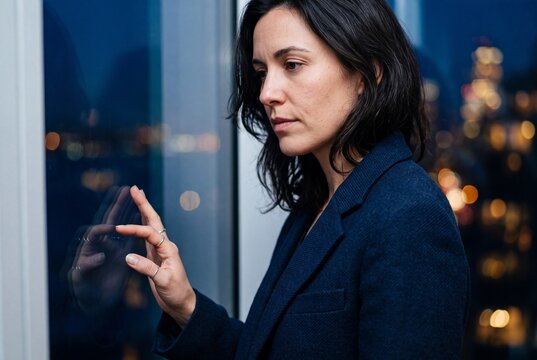 Thoughtful businesswoman touching window glass while looking at city lights at night