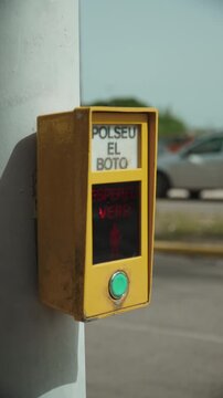 Person presses green button on yellow device of pedestrian crossing activation near road in Spanish city. Organization of smart safe road crossing, system of passage request.
