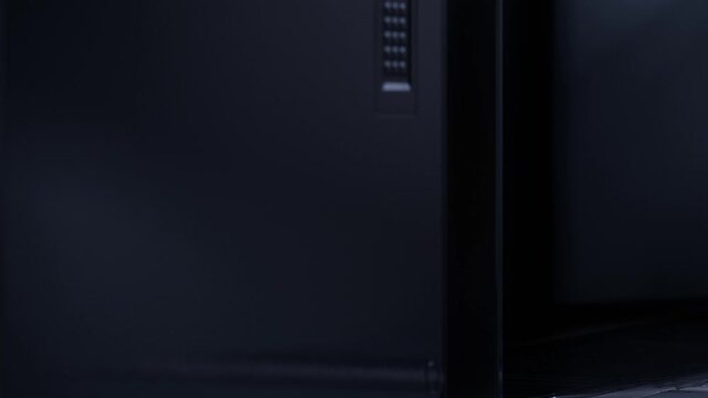 A computer case is placed in a dark room. The design features sleek lines and modern elements. There is a focus on the texture and finish of the case. Lighting creates shadows.