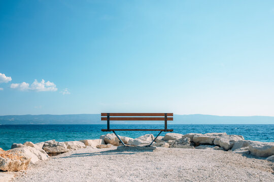 Seaside bench overlooking turquoise sea and distant mountains under a clear blue sky with generous copy space