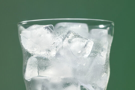A close-up view of a glass filled with ice cubes against green