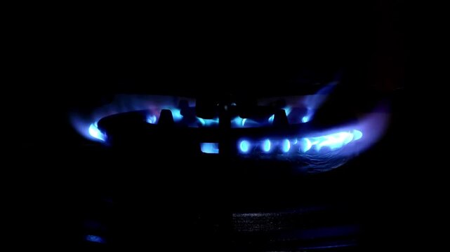 Close-up of a blue gas stove burner flame flickers in the dark. Ideal for energy, cooking, or home concept. Shot with a dark, dramatic low-angle perspective