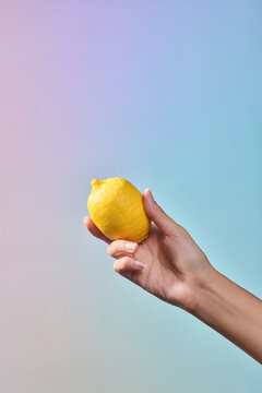 A hand presenting a bright yellow lemon against blue background