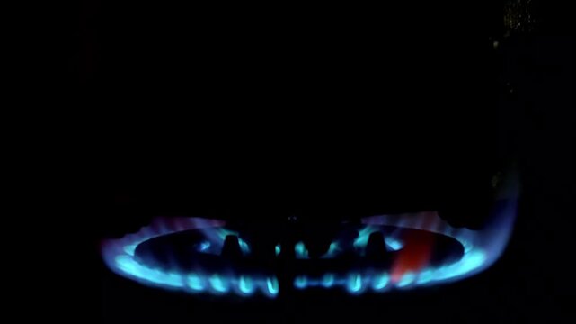 Close-up of a blue gas stove burner flame flickers in the dark. Ideal for energy, cooking, or home concept. Shot with a dark, dramatic low-angle perspective