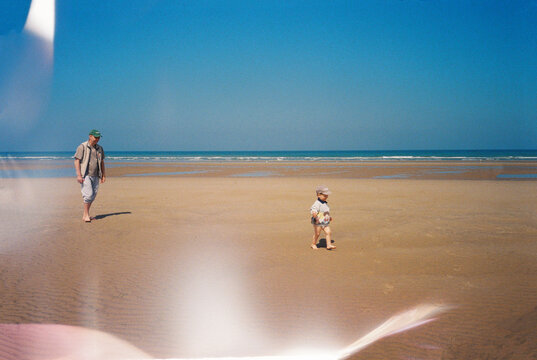 Father and child walking barefoot on a beach at low tide