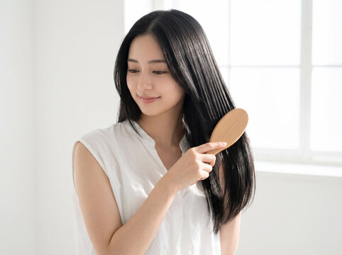 手ぐしのように木製ブラシで髪を整える女性