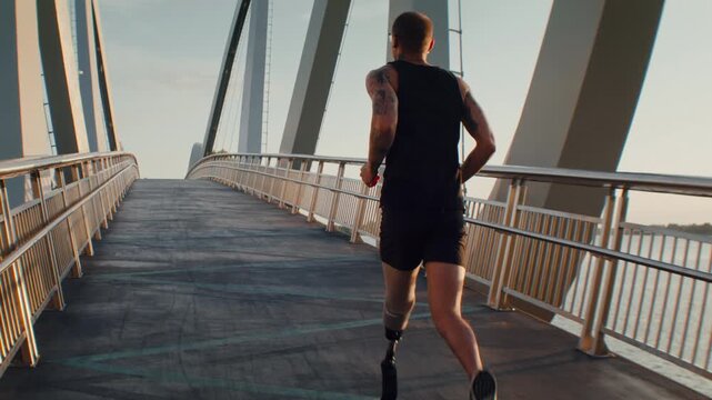 Male runner with leg prosthesis runs across modern footbridge