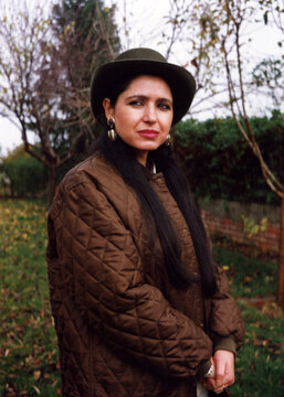 Woman wearing quilted jacket and dark hat in garden
