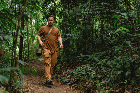 Explorer trekking tropical rainforest path carrying camera lens