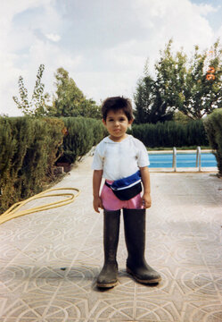 Child wearing oversized boots standing by swimming pool