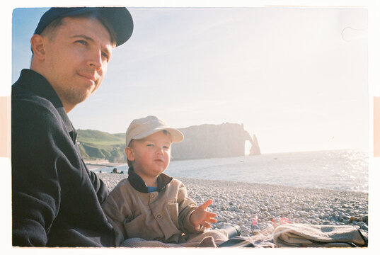 Father and child sitting on Etretat beach in bright sunlight