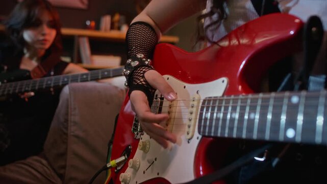 Caucasian teenager plugging cable into red electric guitar and adjusting knobs while friend playing bass guitar in background. Footage ideal for youth lifestyle and music education marketing