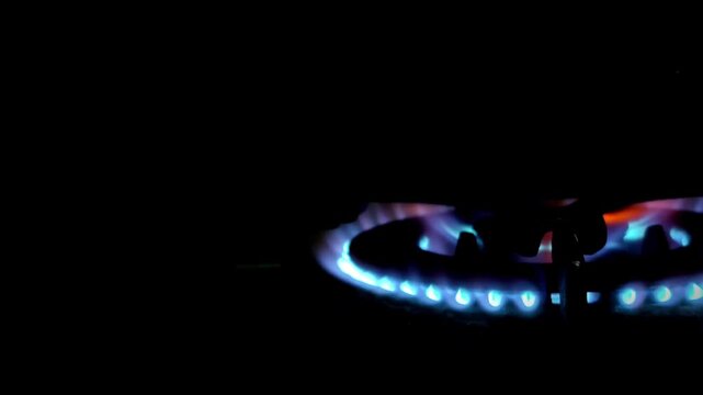 Close-up of a blue gas stove burner flame flickers in the dark. Ideal for energy, cooking, or home concept. Shot with a dark, dramatic low-angle perspective
