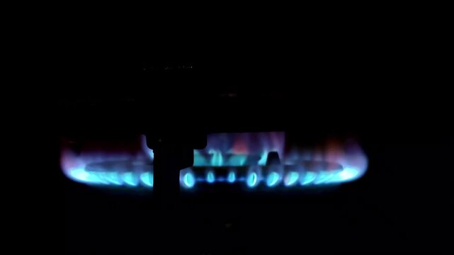 Close-up of a blue gas stove burner flame flickers in the dark. Ideal for energy, cooking, or home concept. Shot with a dark, dramatic low-angle perspective
