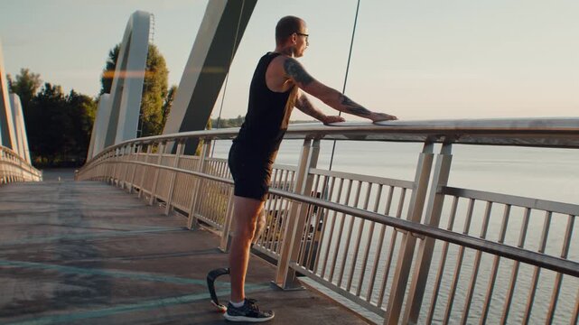 Man with leg prosthesis rests by railing after bridge run