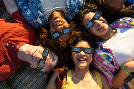 Group of friends with eclipse glasses lying in circle