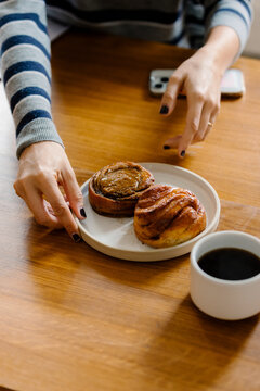 Anonymous person placing a plate of cinnamon rolls next to a cup
