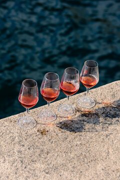 Four red wine glasses in a row on a concrete slab near a sunny river.