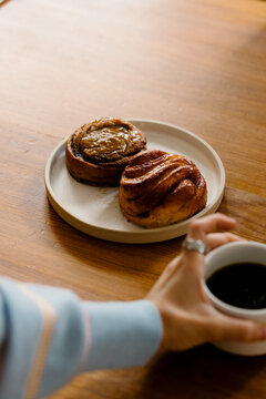 Woman holding a coffee cup next to a plate of cinnamon rolls on wood.