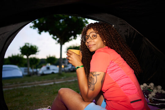 Young woman enjoying coffee inside camping tent outdoors