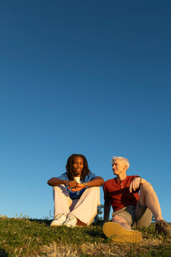 Two male friends sitting on the grass in sunlight 