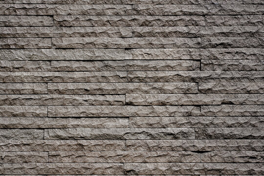 Close up of a dark grey textured stacked stone wall. A modern natural stone veneer cladding surface ideal for architectural and interior design backgrounds.