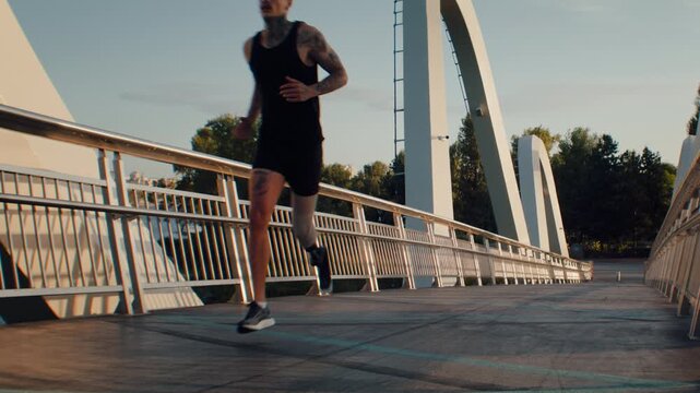 Male runner with leg prosthesis approaching end of wavy bridge