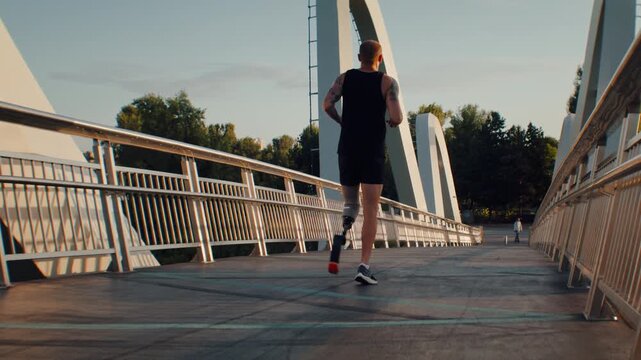 Male athlete with leg prosthesis runs away along bridge