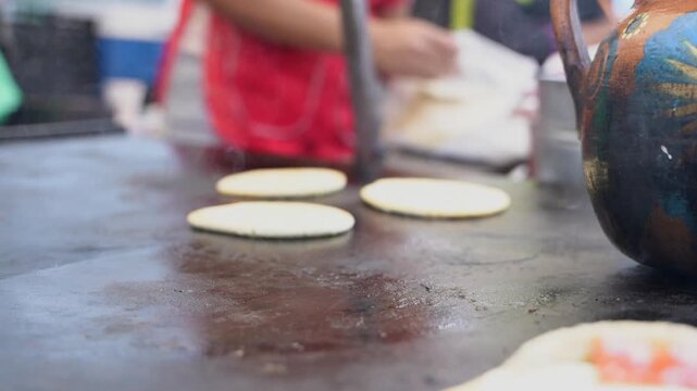 Mexican cook preparing corn tortillas on a comal griddle