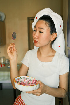 Young asian woman eating, standing indoors with a bowl of salad 