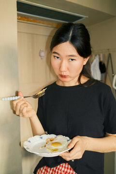 Young beautiful asian woman eating a fried egg for breakfast at home