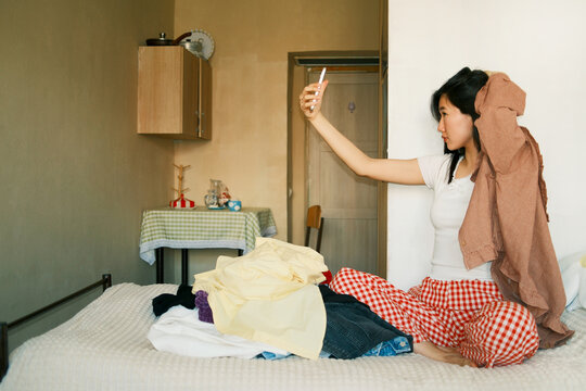 Young asian woman making selfie while sorting clothes and decluttering