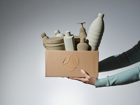 Hands hold a box filled with plastic bottles and containers