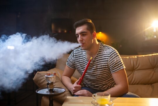 Man exhaling thick smoke rings on a lounge sofa