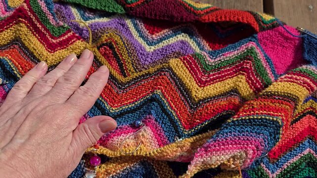 Mature hand lifting colorful natural wool knitted fabric. Norway, Alver. August
