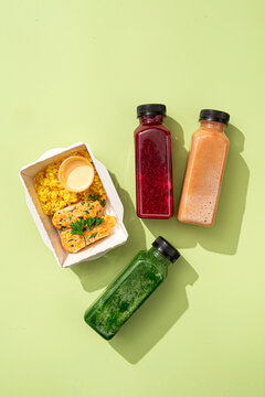 Diet lunch box with rice cutlets sauce and three colorful detox smoothie bottles on pastel green background