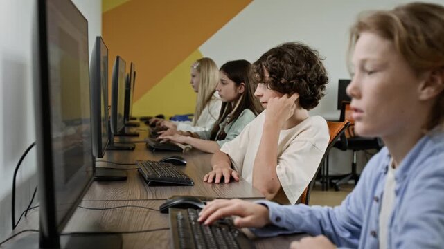 Caucasian teenagers sitting in row in computer lab, typing on keyboards and studying. Footage is ideal for promoting STEM education, coding schools, and modern classroom technology