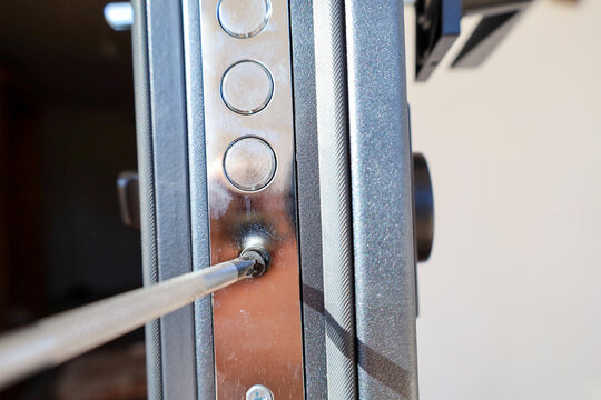 Close-up view of tightening a screw with a screwdriver into the metal faceplate of a door lock. The chrome plate with locking bolts ensures secure mechanism fixation in the entrance door edge.